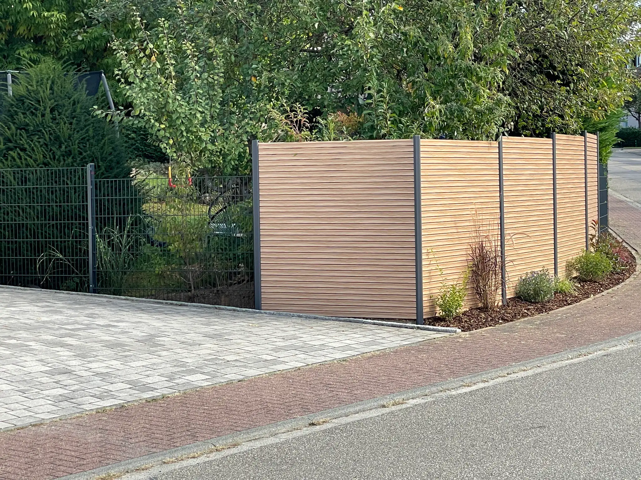 Moderner Sichtschutzzaun in Holzoptik an einer gepflasterten Einfahrt, montiert von HEID ZAUN